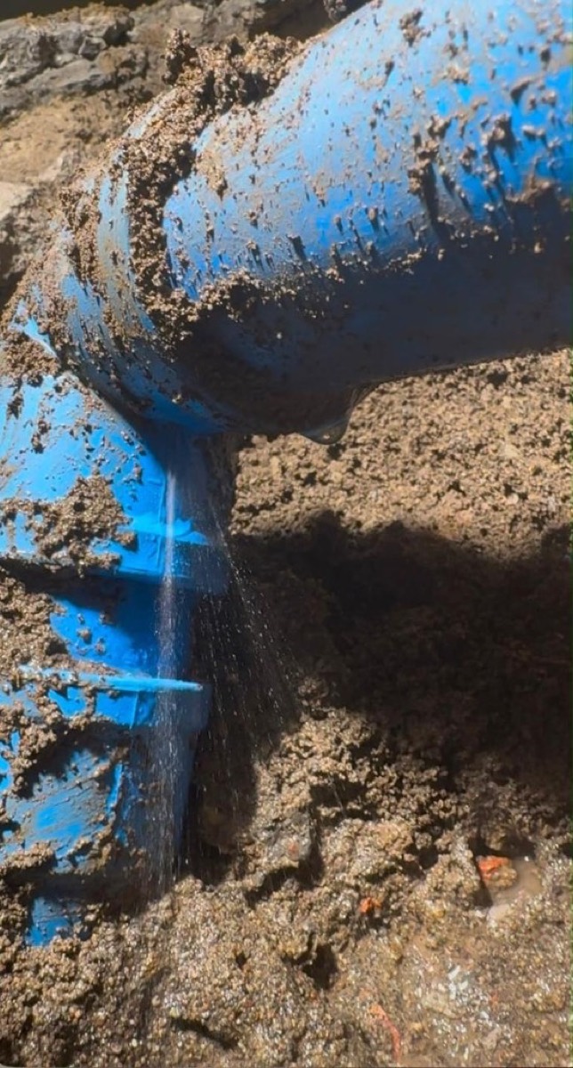 Fuga activa en tubería de PVC azul, con agua saliendo de la unión